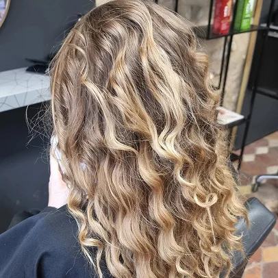 Cheveux blonds bouclés vus de dos, dans un salon de coiffure.