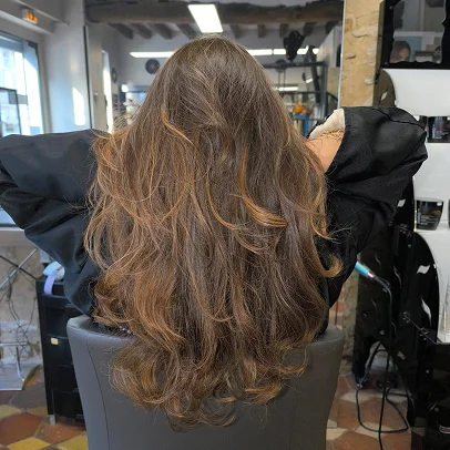Femme aux longs cheveux bruns ondulés dans un salon de coiffure.