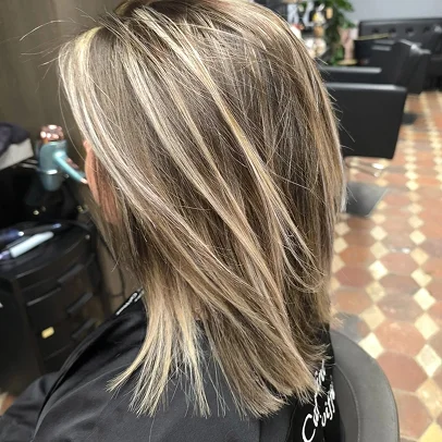 Cheveux châtain clair avec mèches blondes, coupés aux épaules, dans un salon.